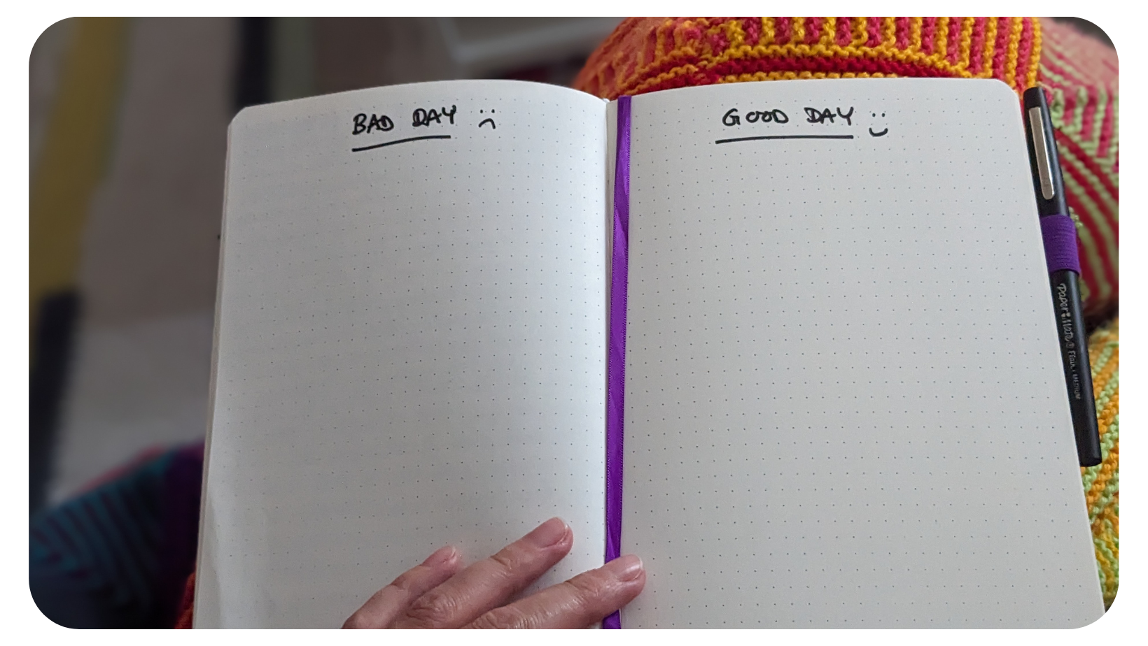 Image shows a notebook open on someone's knee. Their hand is holding the notebook open at a double spread of pages. On the left page there is a handwritten title, 'Bad Day'. On the right page there is a handwritten title, 'Good Day'. The rest of each page is blank ready for a list to be written.